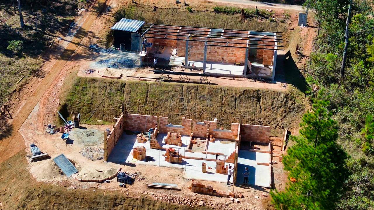 Vista aérea de obra em execução com platôs, alvenaria estrutural e cobertura metálica